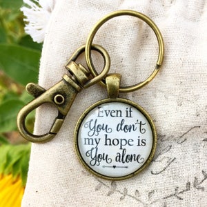 May include: A bronze-colored keychain with a round charm that reads "Even if you don't my hope is you alone".