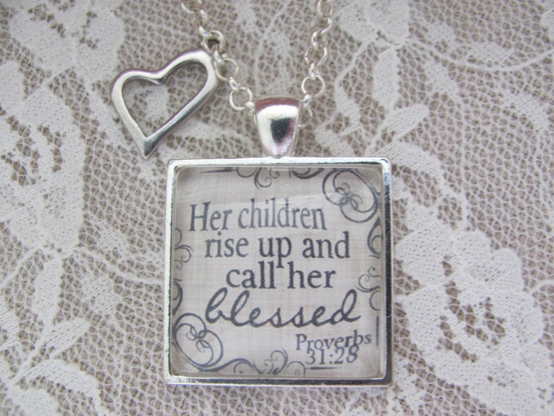 May include: A silver necklace with a heart charm and a square pendant with a quote from Proverbs 31:28. The quote reads "Her children rise up and call her blessed".