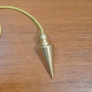 May include: A brass pendulum with a pointed tip and a yellow string.