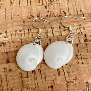 May include: A pair of white shell earrings with silver hooks and chains. The shells have a spiral pattern.