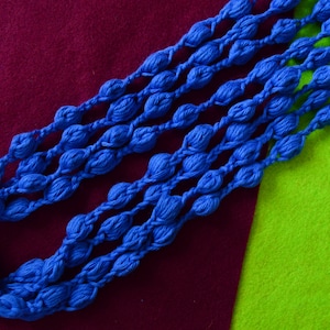 K&ouml;nnte beinhalten: Nahaufnahme einer blauen geh&auml;kelten Halskette aus mehreren Garnstr&auml;ngen. Die Halskette besteht aus kleinen, runden Perlen, die in einem sich wiederholenden Muster miteinander verbunden sind. Die Halskette liegt auf einer roten und gr&uuml;nen Oberfl&auml;che.
