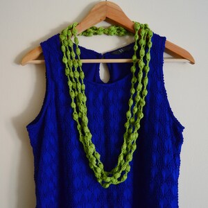 K&ouml;nnte beinhalten: Ein blaues &auml;rmelloses Kleid mit einer gr&uuml;nen Perlenkette, die am Ausschnitt h&auml;ngt.