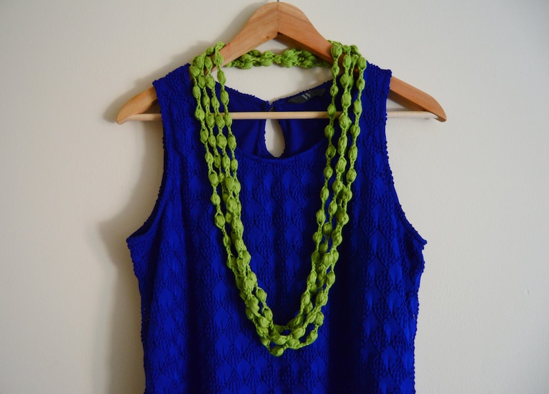 K&ouml;nnte beinhalten: Ein blaues &auml;rmelloses Kleid mit einer gr&uuml;nen Perlenkette, die am Ausschnitt h&auml;ngt.