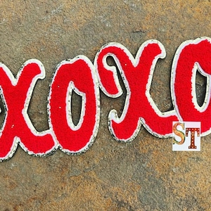 May include: Red felt "XOXO" letters with white outlines and gold glitter accents. The letters are on a brown textured background.