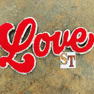 May include: Red felt "Love" sign with white outline and a white "ST" sign below it. The signs are on a brown textured background.