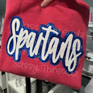 May include: Red sweatshirt with a blue and white sequined "Spartans" design.