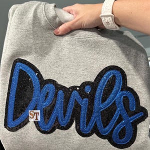May include: Gray sweatshirt with a blue and black sequined "Devils" applique. The applique is in a cursive font.