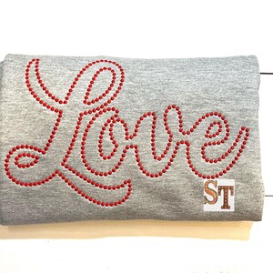 May include: Gray sweatshirt with the word "Love" spelled out in red rhinestones.