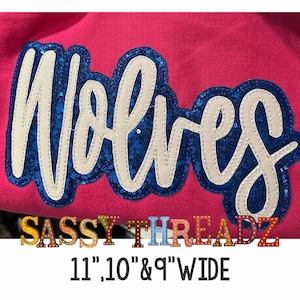 Puede incluir: Tela rosa con una aplicación de "Wolves" de lentejuelas azules y blancas. El texto "SASSY THREADZ" está debajo de la aplicación en letras de colores. El texto "11", "10", y "9" WIDE" está debajo del texto.