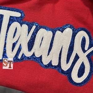 May include: A red fabric patch with the word "Texans" in white letters outlined in blue sequins.