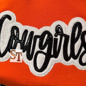 May include: Orange sweatshirt with a white and black sequined patch that says "Cowgirls".