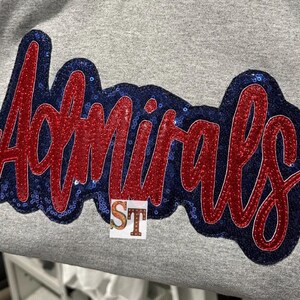 May include: A gray sweatshirt with a red and blue sequined patch that says "Admirals".