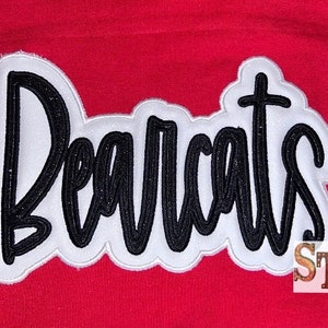 Puede incluir: Parche bordado blanco y negro con la palabra "Bearcats" en una fuente cursiva.