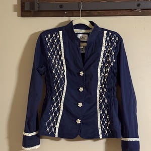 May include: A navy blue jacket with long sleeves, featuring white lace and pearl accents. The jacket has a stand-up collar and decorative flower-shaped buttons. The cuffs and front panels are trimmed with white lace.