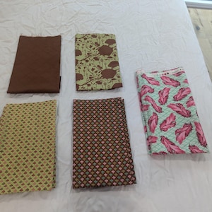 Op de afbeelding: Vijf rechthoekige stukken stof gerangschikt in een raster. Eén is effen bruin, één heeft een bruin en lichtgroen boompjespatroon, één heeft een gele en rode geometrische print, één is bruin met een klein bloemmotief en één heeft roze veren.