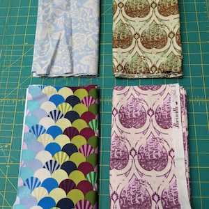 Könnte beinhalten: Vier Stoffmuster mit verschiedenen Mustern. Das obere linke Muster ist hellblau mit einem weißen Blumenmuster. Das obere rechte Muster ist grün mit einem braunen Blumenmuster. Das untere linke Muster ist ein buntes Muster aus sich überlappenden Halbkreisen. Das untere rechte Muster ist ein hellrosa Stoff mit einem violetten Blumenmuster und dem aufgedruckten Text "Parisville" auf der Seite.