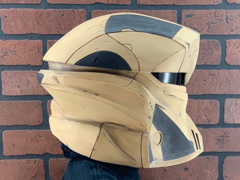 Puede incluir: Un casco futurista beige y gris con un dise&ntilde;o segmentado. El casco presenta una visera oscura y paneles texturizados. La est&eacute;tica general sugiere un tema de ciencia ficci&oacute;n o cosplay.