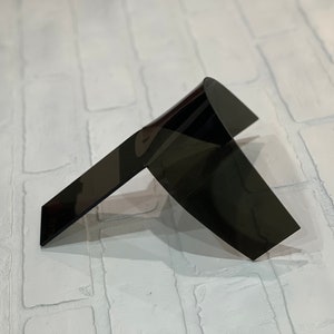 Puede incluir: Una escultura abstracta moderna en negro. La obra presenta dos planos angulados que se cruzan, creando una forma geométrica dinámica. La escultura está hecha de un material oscuro y reflectante, sobre un fondo de ladrillos blancos.