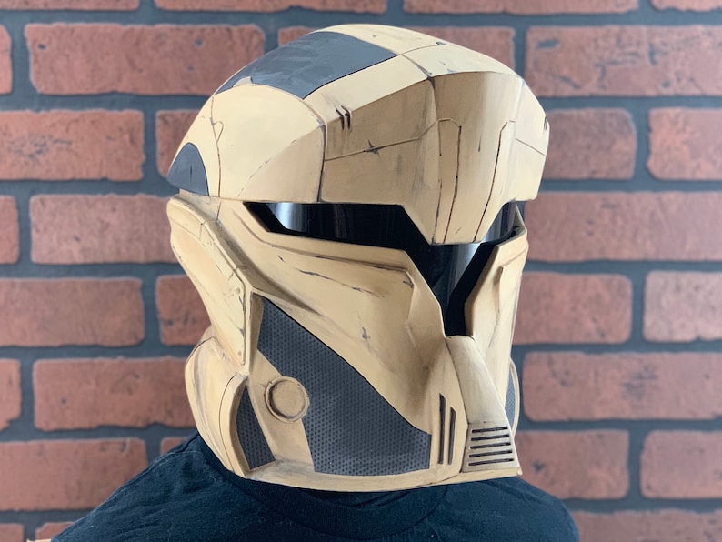 Puede incluir: Un casco futurista en beige y negro con visera. El casco tiene un dise&ntilde;o segmentado con un aspecto texturizado. La visera es oscura y el casco parece estar hecho de un material duradero. El casco est&aacute; dise&ntilde;ado para ser usado.