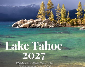 May include: A 12-month wall calendar titled Lake Tahoe 2027 with photography by Angel McNall. The cover features a landscape of turquoise lake water, large light-colored boulders, and tall pine trees against a dark, cloudy sky.