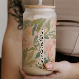 May include: A frosted glass tumbler with a bamboo lid and a clear straw, featuring a watercolor-style floral pattern in shades of pink, green, and cream. The name Samantha is printed vertically in a black script font on the side of the glass.