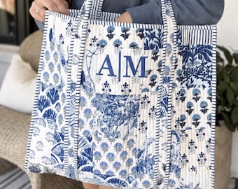 Könnte beinhalten: Eine gesteppte Tragetasche mit blau-weißem Blumenmuster und vertikal gestreifter Verzierung. Auf der Vorderseite sind die Monogrammbuchstaben AM in blauem Garn eingestickt. Die Tasche hat zwei passende gesteppte Schulterriemen.