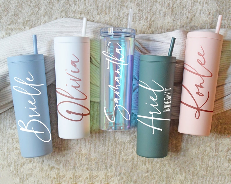 May include: Five personalized stainless steel tumblers with different names and colors. The tumblers are all the same size and have a straw. The names on the tumblers are Brielle, Olivia, Samantha, Ariel Bridesmaid, and Romlee.