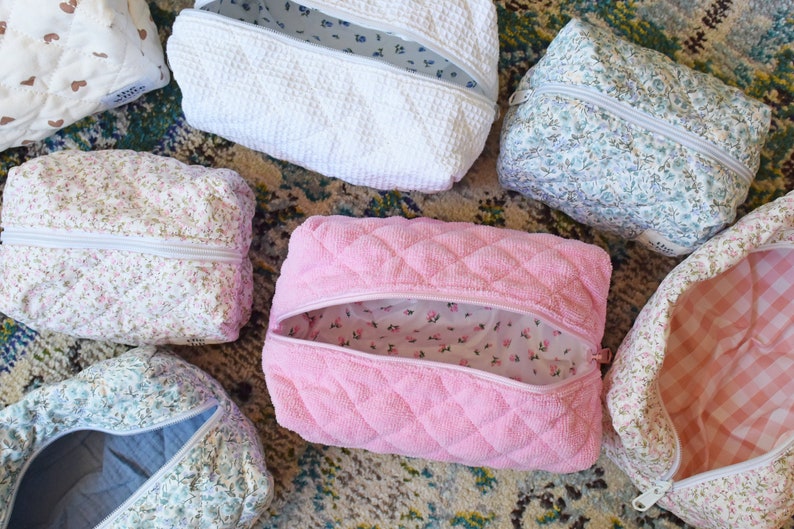 May include: Assortment of quilted makeup bags in various floral patterns and colors, including pink, white, and blue. The bags have zipper closures and are perfect for organizing toiletries or other small items.