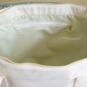 May include: A white canvas tote bag with a zippered pocket on the inside. The bag has two handles.