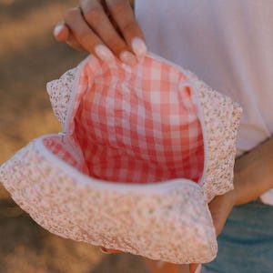 May include: A white and pink floral print makeup bag with a pink and white gingham lining. The bag is open and the lining is visible.