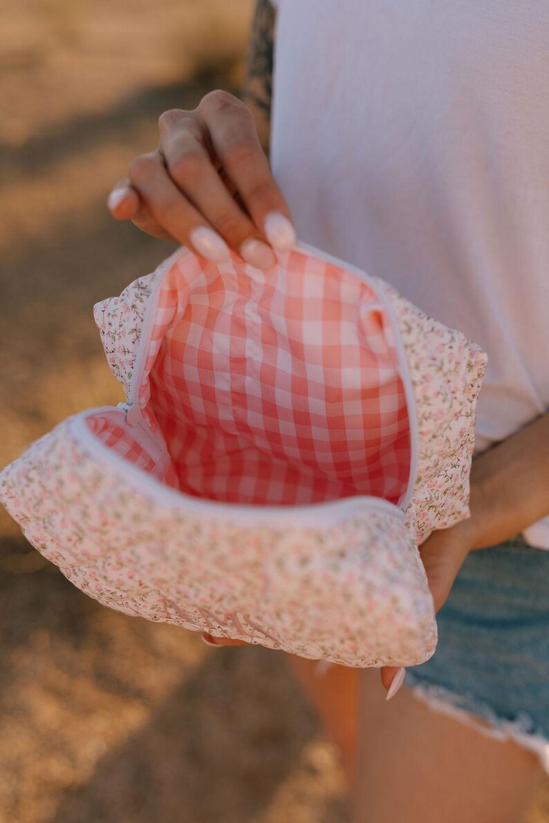 May include: A white and pink floral print makeup bag with a pink and white gingham lining. The bag is open and the lining is visible.