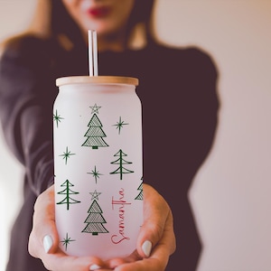 K&ouml;nnte beinhalten: Vereister Glasbecher in Dosenform mit Bambusdeckel und Strohhalm. Der Becher ist mit gr&uuml;nen Weihnachtsb&auml;umen und Sternen verziert. Der Name "Samantha" ist in roter Schrift auf der Seite geschrieben.
