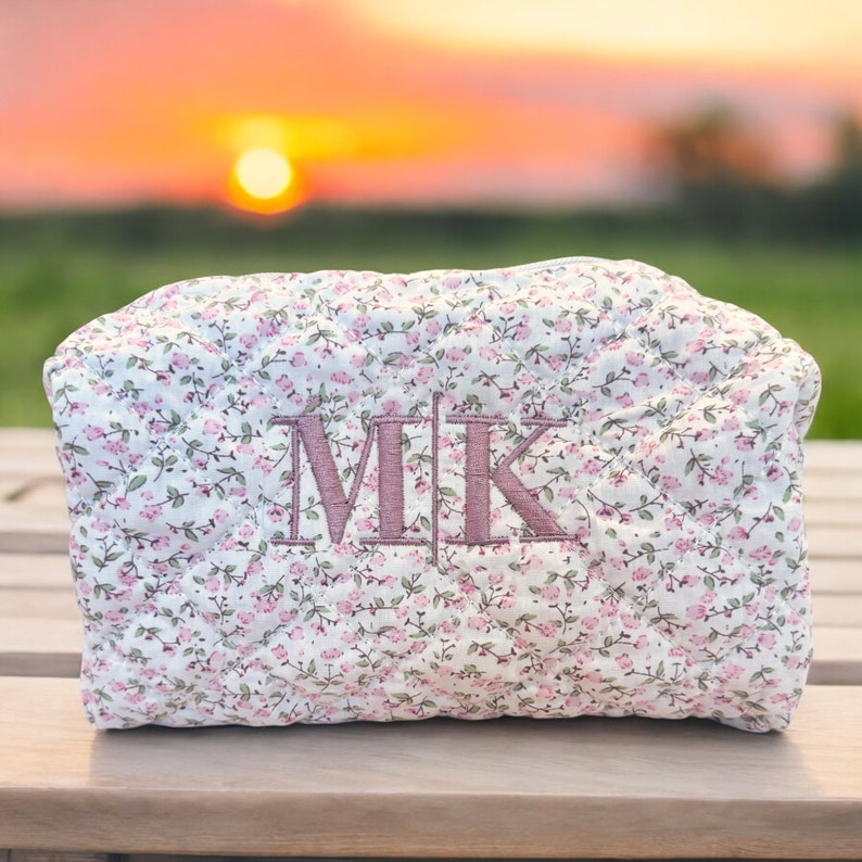 May include: A white quilted makeup bag with a pink floral pattern and the initials "M.I.K." embroidered in pink.