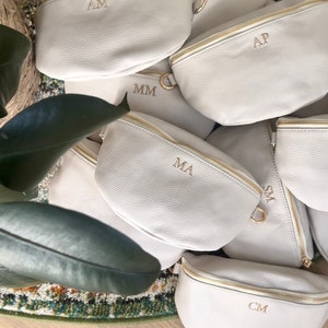 K&ouml;nnte beinhalten: Eine Gruppe von cremefarbenen Bauchtaschen mit goldenen Rei&szlig;verschl&uuml;ssen und personalisierten Initialen. Die Initialen sind AM, FW, AP, MM, MA, SM und CM.