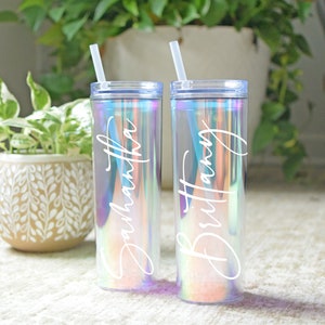 May include: Two iridescent tumblers with clear straws. The tumblers have the names "Samantha" and "Brittany" written on them in white.
