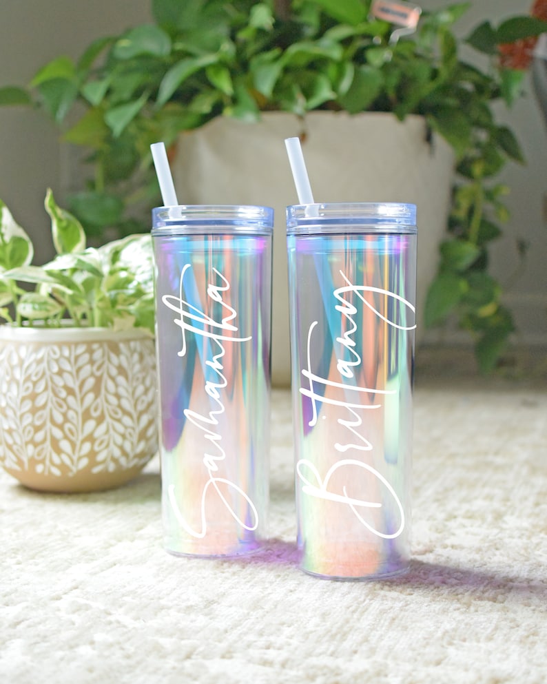 May include: Two iridescent tumblers with clear straws. The tumblers have the names "Samantha" and "Brittany" written on them in white.