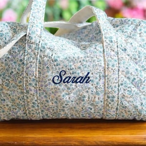 May include: A white and blue floral print duffel bag with a white strap and the name "Sarah" embroidered in blue.