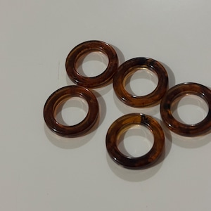 May include: Five brown, translucent, circular rings with a tortoiseshell pattern. The rings are evenly spaced and appear to be made of a glossy material. The color is a mix of amber and dark brown.