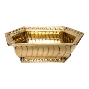 May include: A rectangular, gold-colored metal planter with an octagonal shape. The planter features a decorative, ribbed design on the sides and a beaded trim along the top and bottom edges. The interior is smooth and reflective.