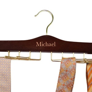 May include: A dark brown wooden tie hanger with a gold hook and metal tie clips. The hanger is personalized with the name "Michael".