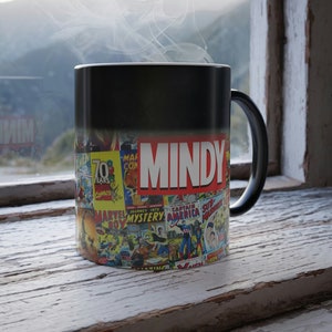 May include: Black magic mug with a colorful comic book design featuring the name "MINDY" printed on the front. Steam is rising from the mug.