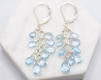 May include: Silver dangle earrings with multiple light blue teardrop-shaped gemstones hanging from each earring.