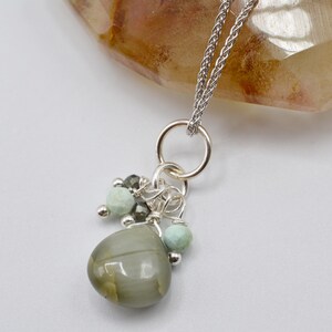 May include: A silver chain necklace with a gray stone pendant and small green and gray beads.