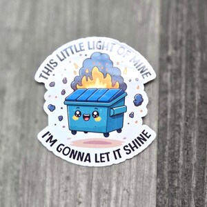 May include: A white sticker with a blue trash can with a smiling face on fire. The text on the sticker reads "This little light of mine I'm gonna let it shine."