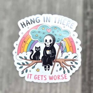 May include: A sticker with a rainbow, a cloud, a black cat, and a skeleton holding a cup of coffee. The text reads "Hang in there it gets worse".