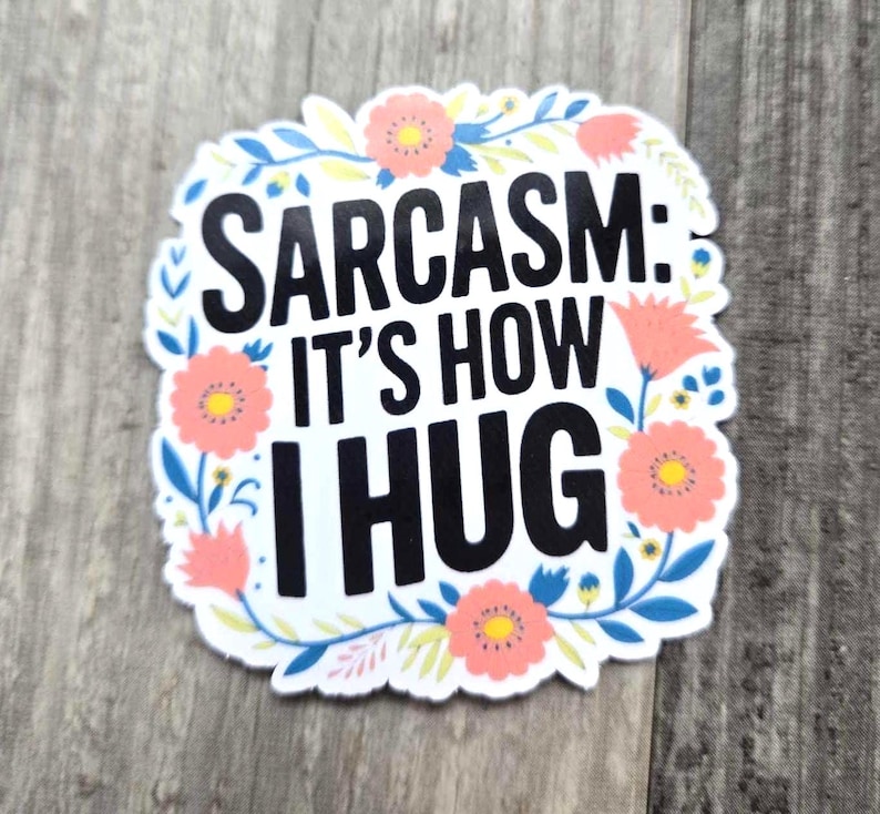 May include: White sticker with a floral border and the text "Sarcasm: It's how I hug" in black.
