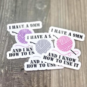 May include: A collection of white stickers with text and graphics related to crochet. Each sticker features the phrase "I HAVE A 9MM" above a yarn ball and crochet hook design, with the text "AND I KNOW HOW TO USE IT" below.