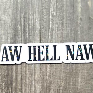 May include: A white sticker with the phrase "AW HELL NAW" in black capital letters. The letters have a holographic, star-like design. The sticker is on a gray wooden surface.