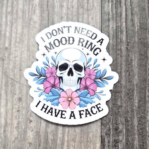 May include: White sticker with a black skull with flowers and the text "I don't need a mood ring I have a face".
