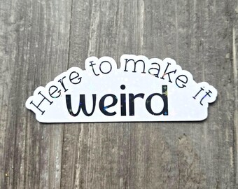 Könnte beinhalten: Ein weißer Aufkleber mit dem Text "Here to make it weird" in einer schwarzen, verspielten Schriftart. Das Wort "weird" hat einen glitzernden, mehrfarbigen Effekt. Der Aufkleber befindet sich auf einer Holzoberfläche.